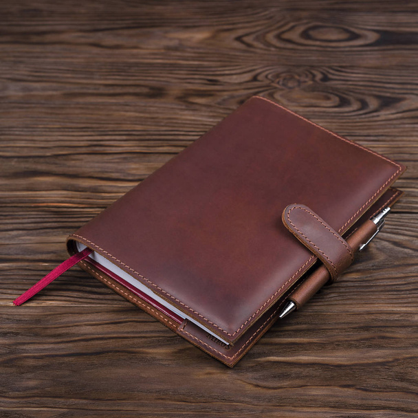 Red color handmade leather notebook cover with notebook and pen inside on wooden background. Stock photo of luxury business accessories. - Fotoğraf, Görsel