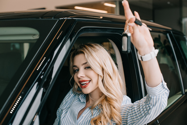 selective focus of happy young woman holding car key while sitting in automobile  - 写真・画像