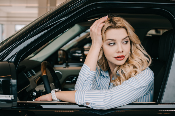 beautiful blonde woman sitting in automobile in car showroom  - Фото, изображение