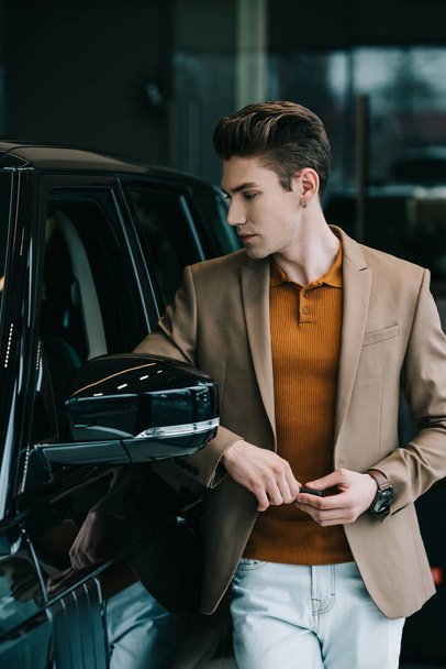 handsome man looking at black automobile in car showroom  - Fotó, kép