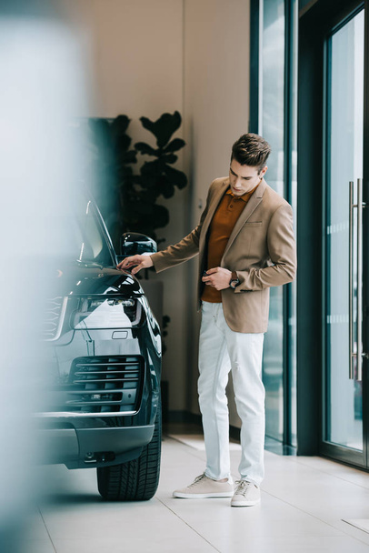 selective focus of handsome man looking at black automobile in car showroom  - Foto, immagini