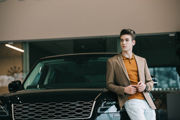 handsome man standing near automobile in car showroom  - Valokuva, kuva