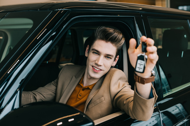 selective focus of happy man holding car key while sitting in automobile  - Photo, Image