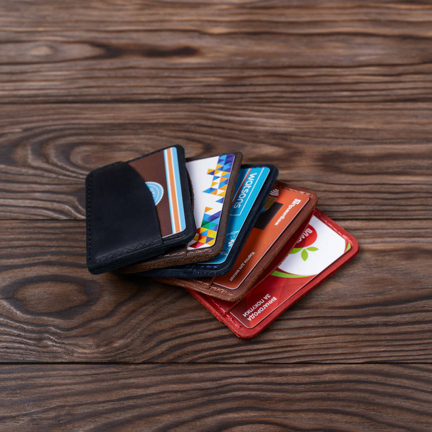 Ukraine, Kyiv, 20.02.2019 Five two pocket handmade leather cardholders with cards inside on wooden background. Editorial use only - Фото, изображение