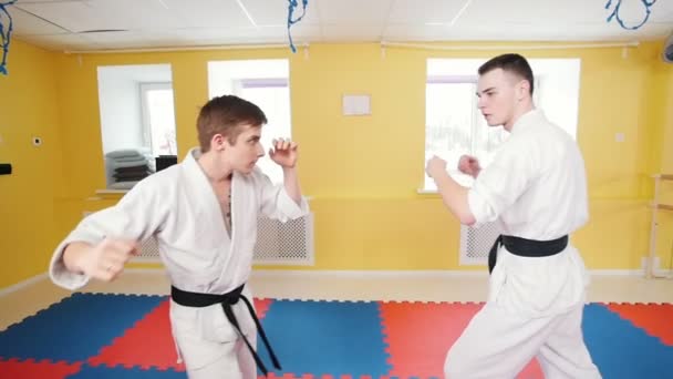 Kampfkunst. Zwei sportliche Männer trainieren ihre Aikido-Fähigkeiten im hellen Studio. pariert den Treffer und wirft den Gegner auf den Boden - Filmmaterial, Video
