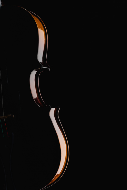 κοντά στο κλασικό ξύλινο βιολοτσέλο στο σκοτάδι απομονώνεται σε μαύρο - Φωτογραφία, εικόνα