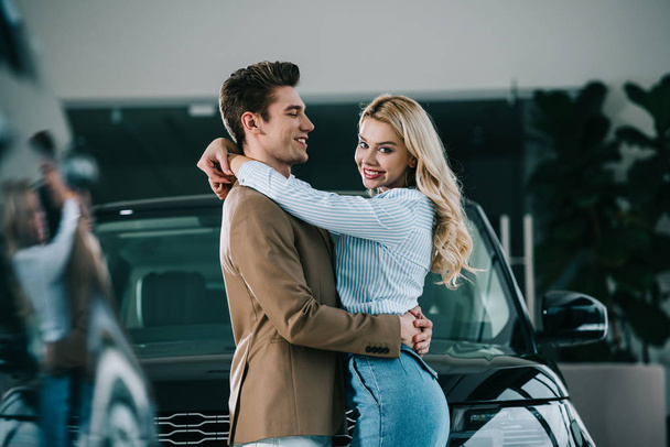 beautiful blonde girl hugging happy man while standing near car  - Foto, imagen