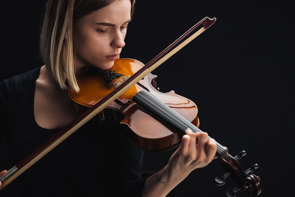 молодая сконцентрированная женщина играет на виолончели с луком, изолированным на черном
 - Фото, изображение