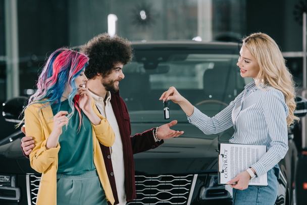 aantrekkelijke blonde auto dealer geven sleutel tot gelukkige man en vrouw  - Foto, afbeelding
