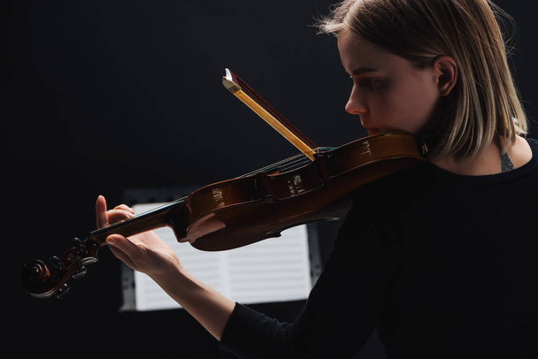 foyer sélectif de jeune femme concentrée jouant du violoncelle avec arc dans l'obscurité avec livre de musique à l'arrière-plan isolé sur noir
  - Photo, image