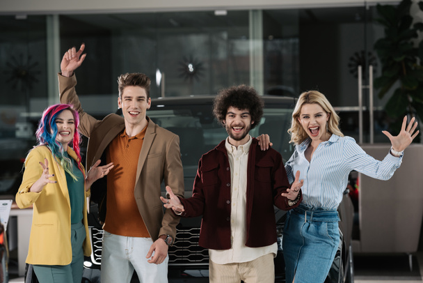happy group of friends gesturing near automobile in car showroom  - Photo, Image