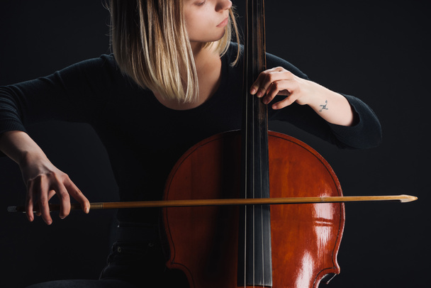 partial view of tattooed woman playing double bass in darkness isolated on black - Photo, Image