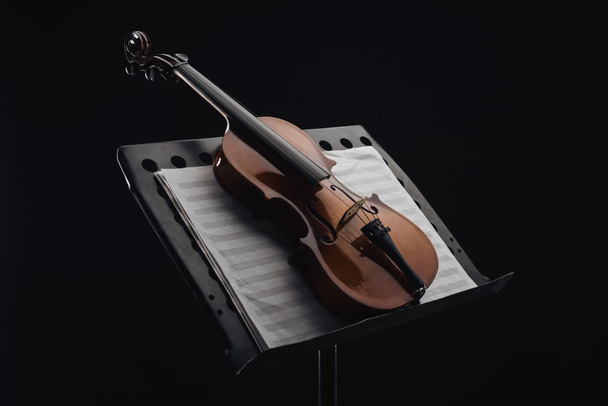 classic wooden cello on opened music book on stand isolated on black  - Foto, imagen