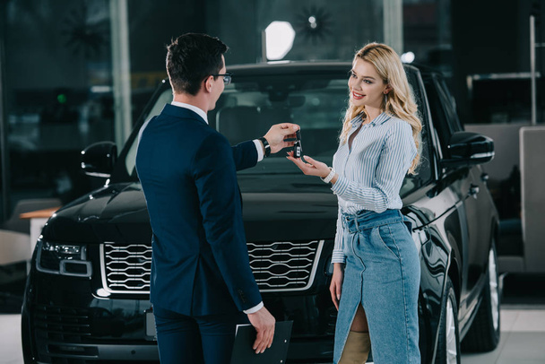 back view of car dealer giving key to happy blonde girl  - Photo, Image