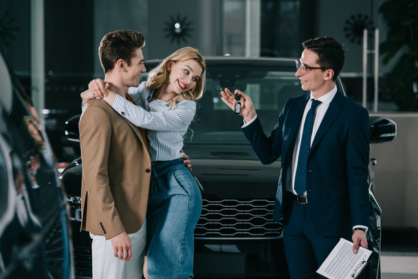 handsome car dealer giving key to happy blonde woman hugging man  - Foto, immagini