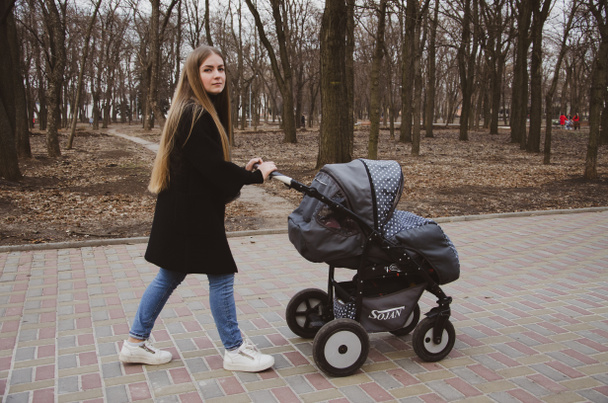 Мать с коляской прогуливается по аллее в парке в течение дня
 - Фото, изображение
