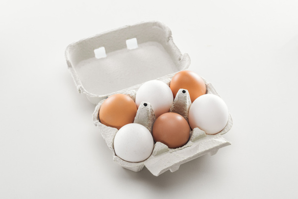 rauwe witte en bruine kippeneieren in kartonnen doos op witte achtergrond - Foto, afbeelding
