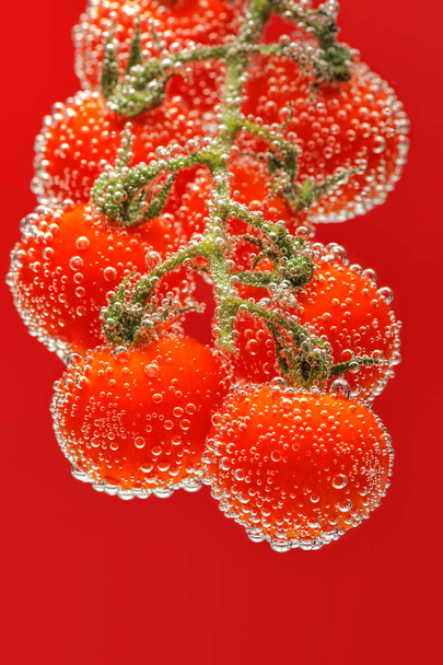 Ripe red cherry tomatoes on branch submerged in water with bubbles. Bright smooth red background. - Fotoğraf, Görsel