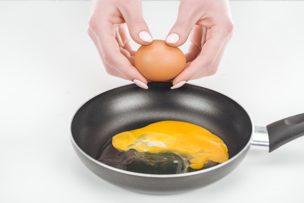 vista parcial de la mujer preparando huevos revueltos en sartén sobre fondo blanco
 - Foto, Imagen