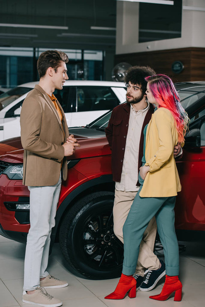 komea mies puhuu ystävien kanssa lähellä autoja autossa showroom
  - Valokuva, kuva