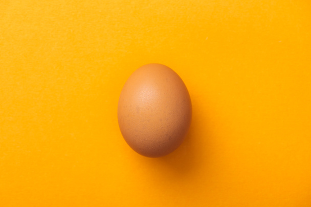 Widok z góry całego brązowego jaja kurzego na jasnym pomarańczowym tle - Zdjęcie, obraz