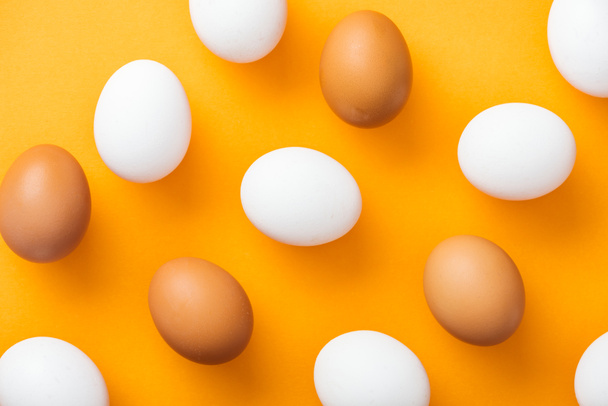 top view of whole white and brown fresh chicken eggs on bright orange background  - Foto, imagen