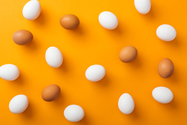 top view of whole white and brown organic chicken eggs on bright orange background  - Foto, Bild