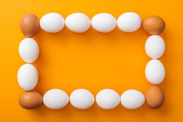 top view of whole white and brown organic chicken eggs arranged in square frame on bright orange background with copy space - Fotoğraf, Görsel