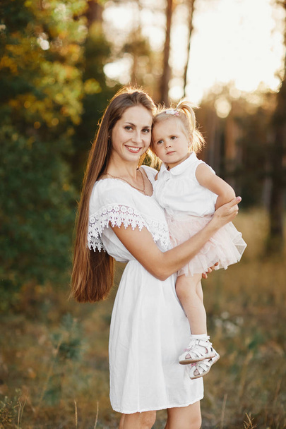 Porträt von Mutter und Tochter. kleines Mädchen mit zwei Schwänzen. Mutter hält auf einer Wiese ein kleines Mädchen im Arm - Foto, Bild
