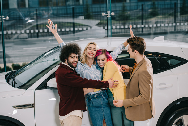 cheerful group of friends hugging with attractive blonde girl near white car  - Foto, Bild