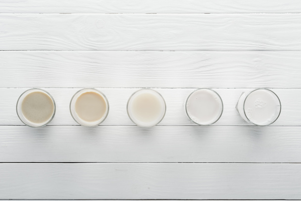 bovenaanzicht van verschillende soorten melk op wit houten oppervlak - Foto, afbeelding