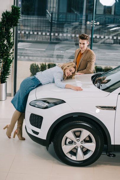 handsome man looking at attractive happy girl touching white car  - Fotoğraf, Görsel