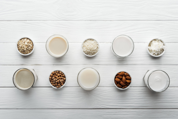 top view of glasses with coconut, chickpea, oat, rice and almond milk on white wooden table with ingredients in bowls - Photo, Image