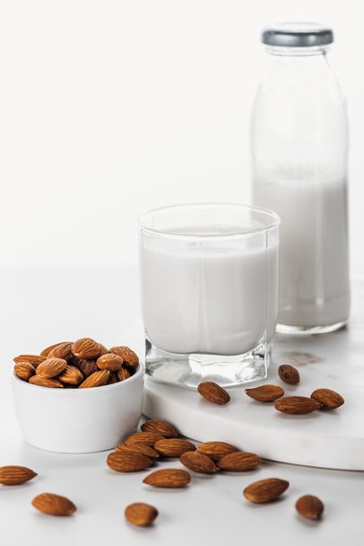 mandlové mléko v láhvi a sklo v blízkosti ořechů v nádobě izolované na bílém - Fotografie, Obrázek