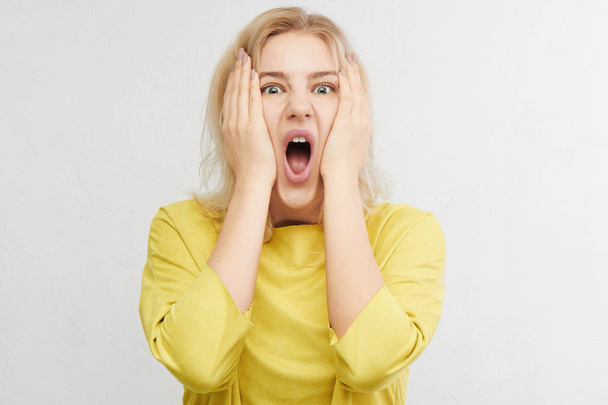 Woman in horror holds head with hands and screams of fear, anger and surprise isolated on white background. Something terrible and unexpected happened, expressive emotions - Foto, imagen