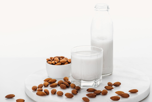 vegan white almond milk in bottle and glass near nuts in bowl isolated on white - Foto, Bild