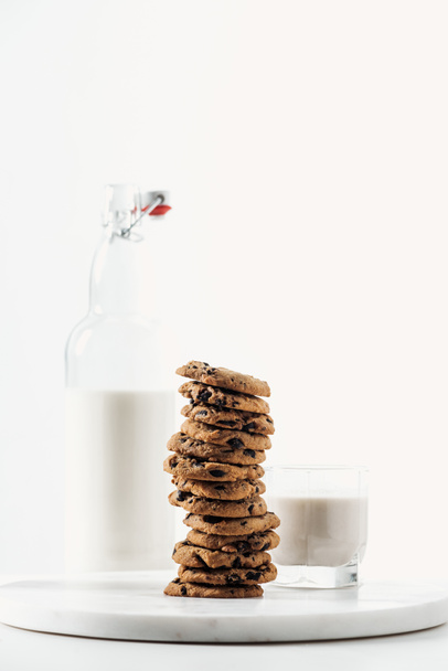fresh milk in glass and bottle near chocolate cookies on marble stand isolated on white - Foto, imagen