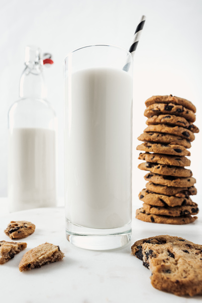 selective focus of glass with fresh milk and straw near chocolate cookies and bottle on marble table - Photo, image