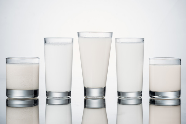 row of glasses with organic fresh alternative milk on grey background with reflection - Photo, Image