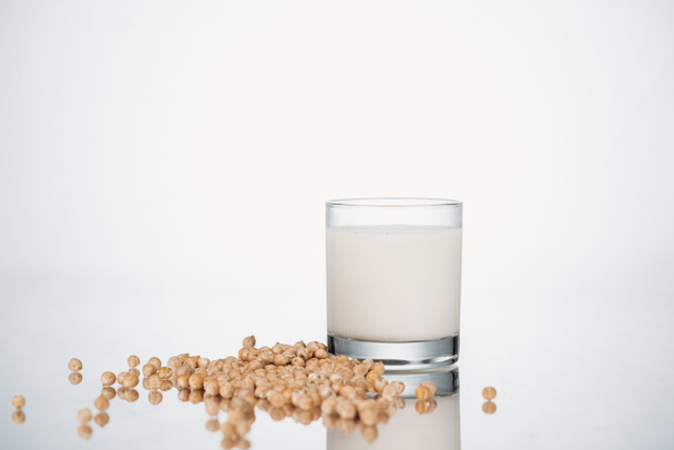 chickpea vegan milk in glass near scattered beans on grey background - Foto, afbeelding