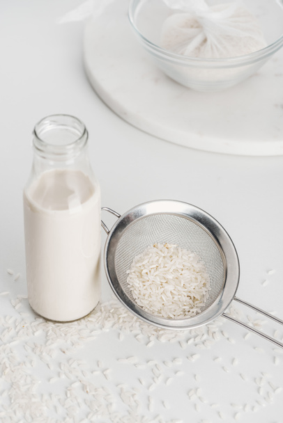 selective focus of rice milk in bottle near rice and sieve with rice in cheesecloth on background - Photo, image