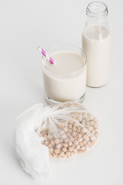 chickpea in white cheesecloth near bottle and glass with vegan chickpea milk on grey background - Fotografie, Obrázek