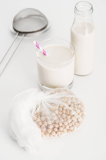 chickpea in white cheesecloth near bottle and glass with vegan chickpea milk and sieve on grey background - Photo, Image