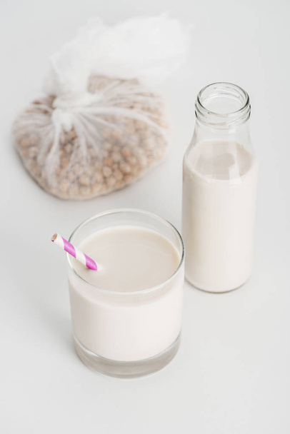 kikkererwten in kaasdoek bij fles en glas met veganistische kikkererwten melk op grijze achtergrond - Foto, afbeelding