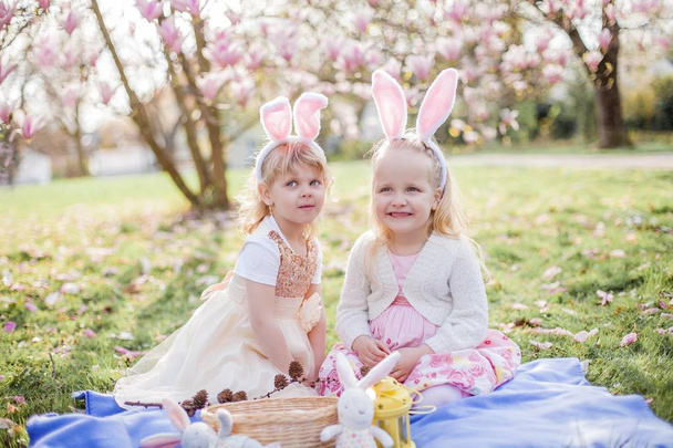 Küçük sevimli kızlar mogolia yakın çim üzerinde oturuyor. Kostüm Paskalya tavşanlar kızlar. - Fotoğraf, Görsel