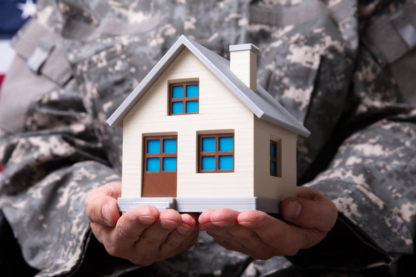 Mid Section Of Soldier Holding Model House In Hand - Foto, Imagen