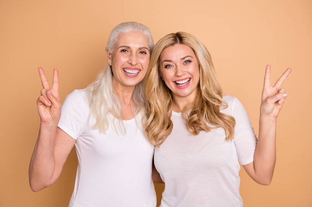 Portrait of nice-looking lovely winsome sweet attractive charming cute cheerful cheery positive ladies wearing white t-shirt showing v-sign isolated over beige pastel background - Photo, image