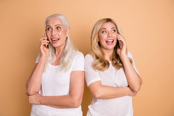 Portrait of nice-looking lovely adorable attractive charming cute cheerful cheery glad ladies wearing white t-shirt talking with boyfriend roaming cellular isolated over beige pastel background - Photo, image