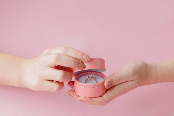 Woman opens a gift box with jewellery. Wedding ring in a box in the hands of women on a pink background - Foto, imagen