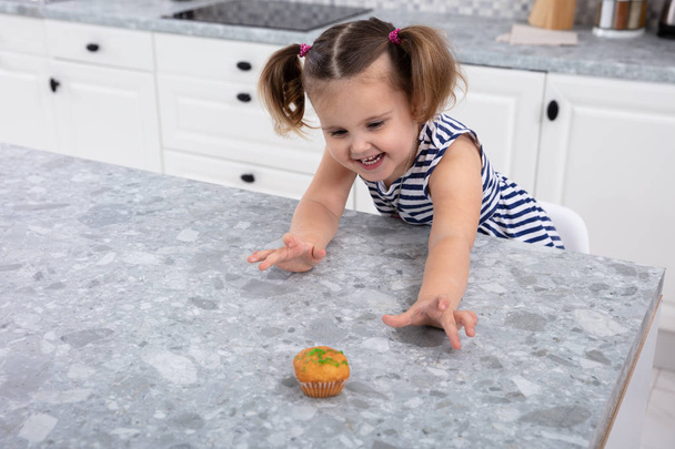 Smiling Cute Girl's Hand Reaching For Cupcake On Kitchen Counter - Fotó, kép
